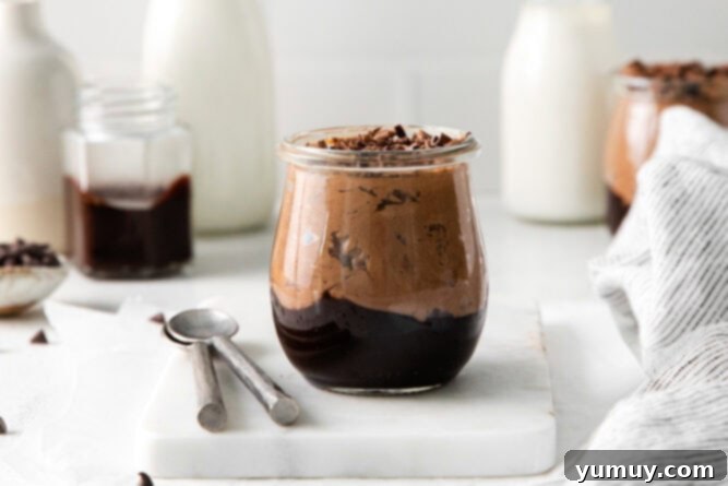 side view of a no bake chocolate cheesecake cup on a marble cutting board with spoons.