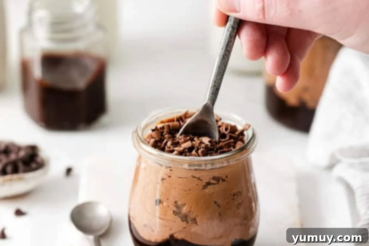 dipping a spoon into a serving of chocolate cheesecake mousse topped with chocolate curls.
