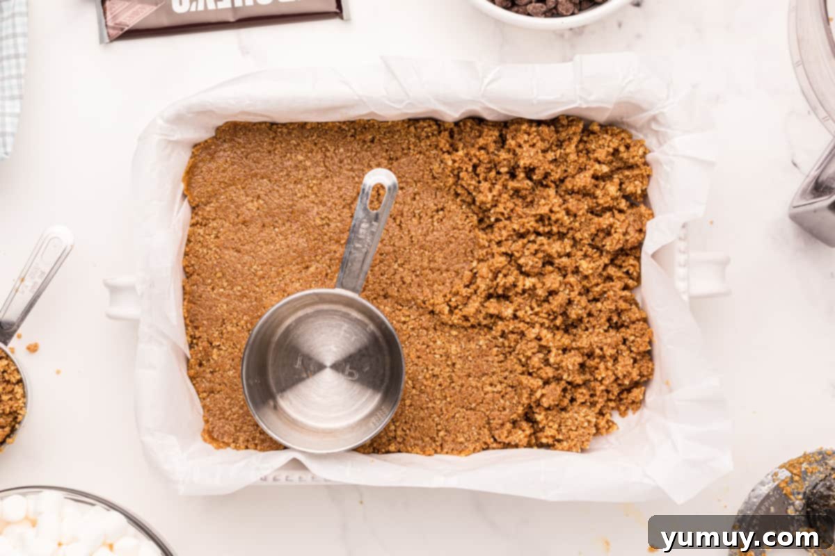 Smores Bars 17 pressing graham cracker crust into a baking pan with a measuring cup.