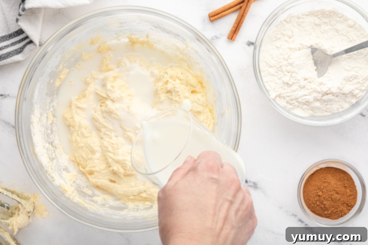 pouring buttermilk into cupcake batter in a glass bowl.