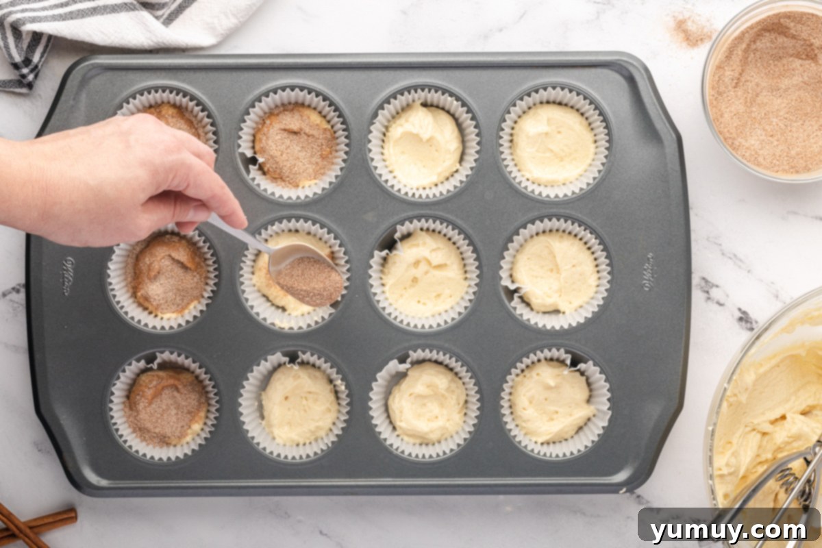 spooning cinnamon sugar over half-filled cupcakes in a lined cupcake tin.