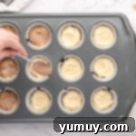 spooning cinnamon sugar over half-filled cupcakes in a lined cupcake tin.