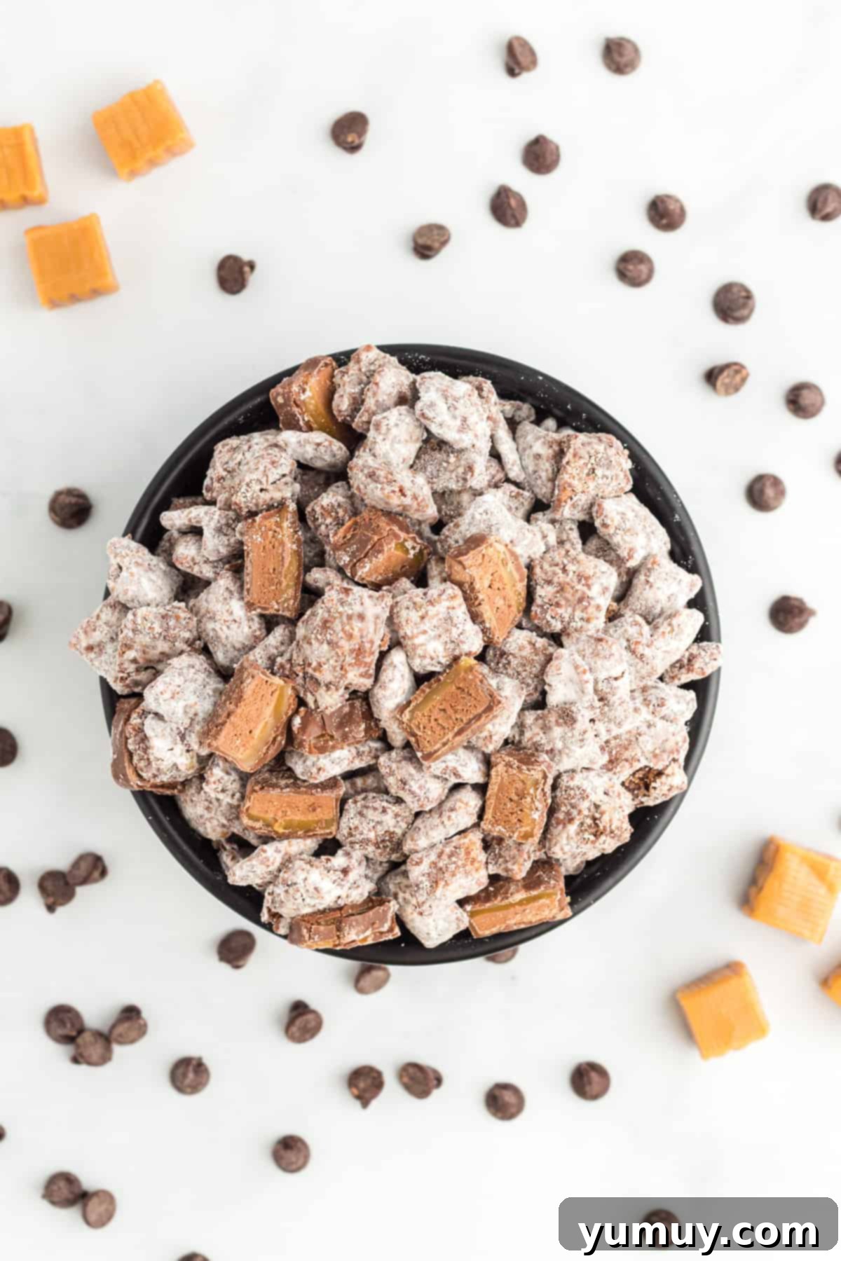 overhead view of Milky Way puppy chow in a bowl, surrounded by chocolate chips and caramels