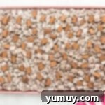 puppy chow spread out on a baking tray, with chocolate caramels dotted throughout