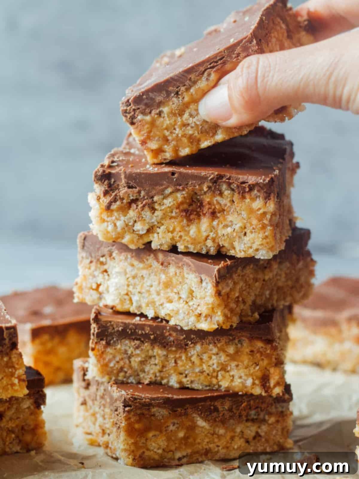 Hand picking up a scotcheroo off the top of a stack, showcasing the delicious chocolate and butterscotch topping.