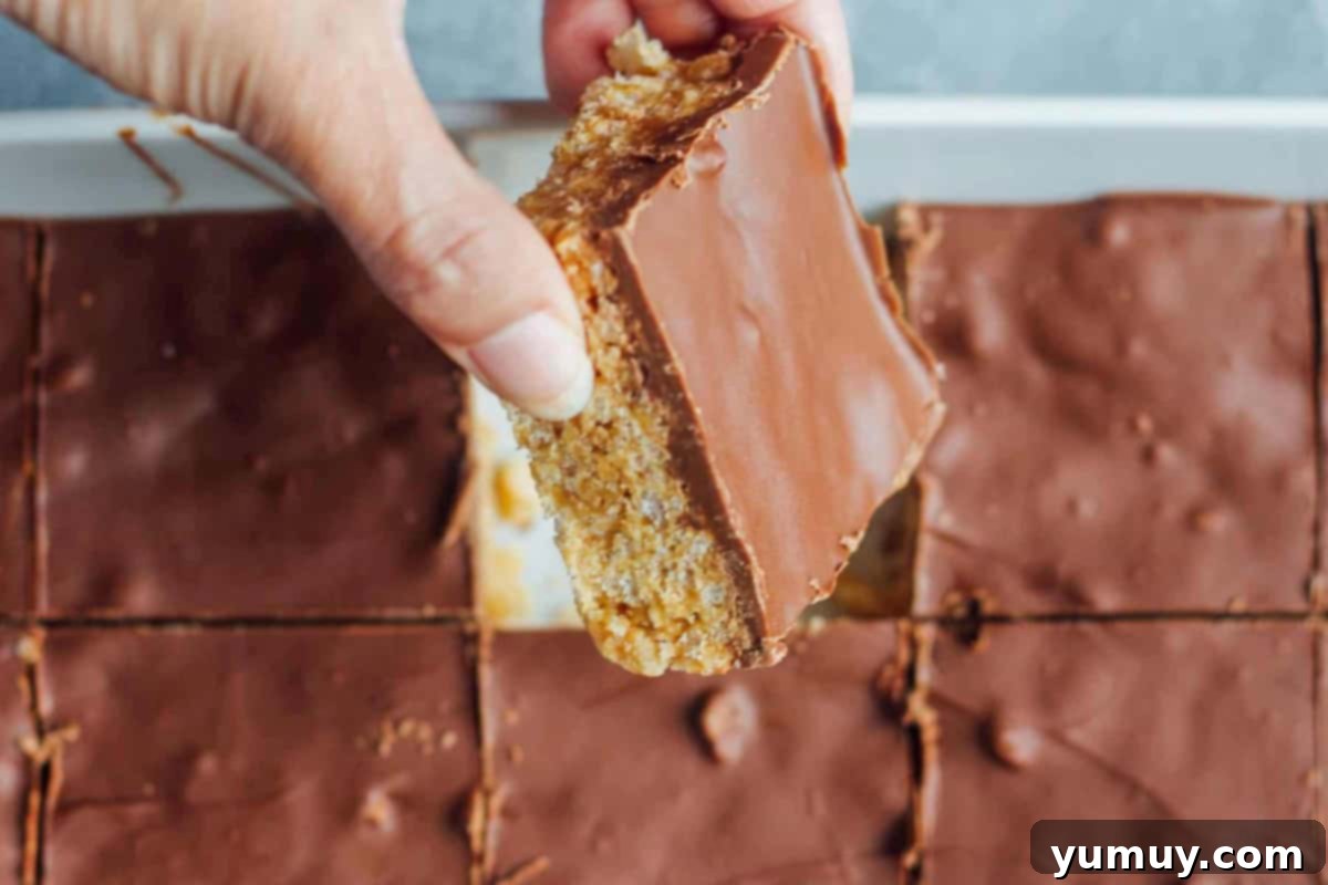 Hand lifting a perfectly gooey scotcheroo bar from a baking pan, showing its irresistible texture.