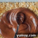 A spoon drizzling melted chocolate and butterscotch over a tray of scotcheroos.