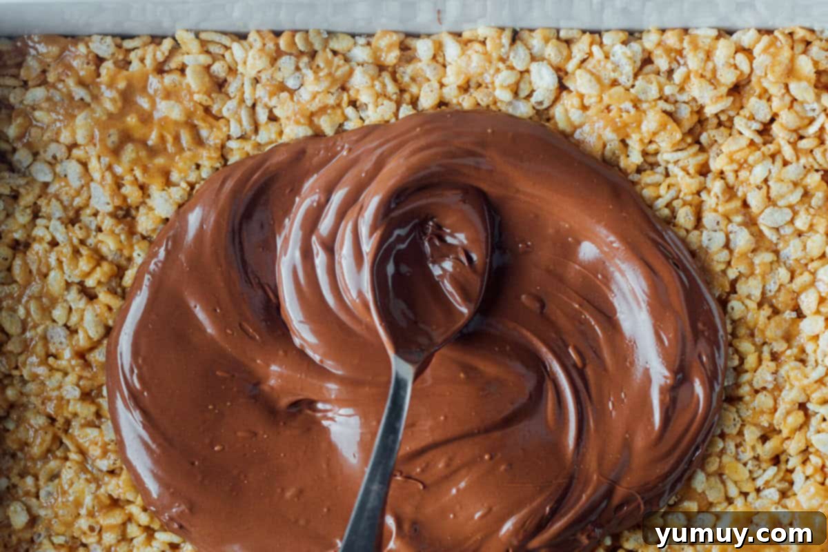 A spoon drizzling melted chocolate and butterscotch over a tray of granola bars, creating a rich topping.