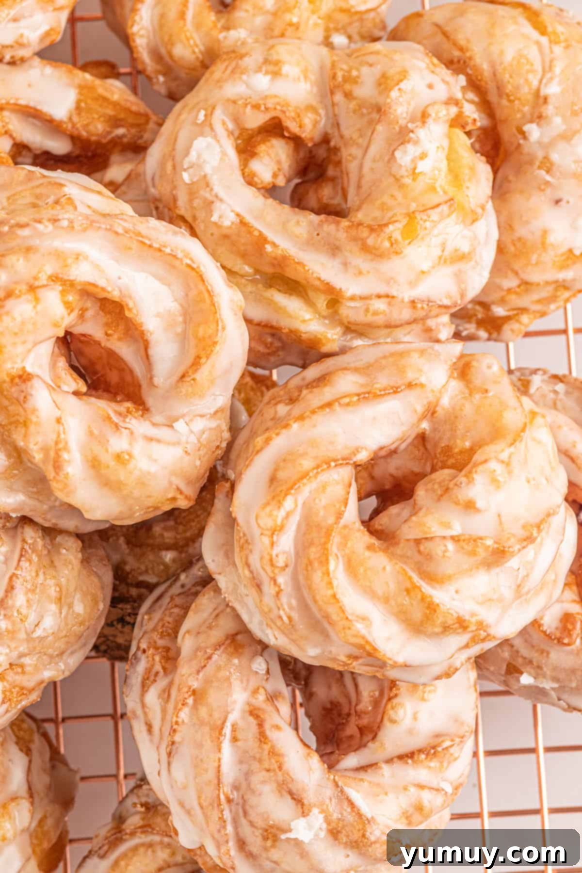 Two golden-brown French crullers with a shiny vanilla glaze, resting on a white plate, showcasing their iconic ridged texture.