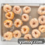 Warm French crullers arranged on a cooling rack, freshly dipped in vanilla glaze and allowing excess to drip.