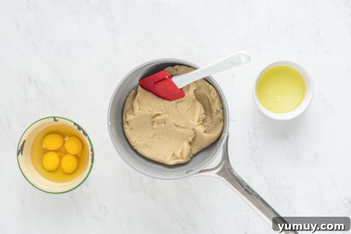 A mixing bowl containing the cooked choux pastry dough, with additional eggs and butter nearby.