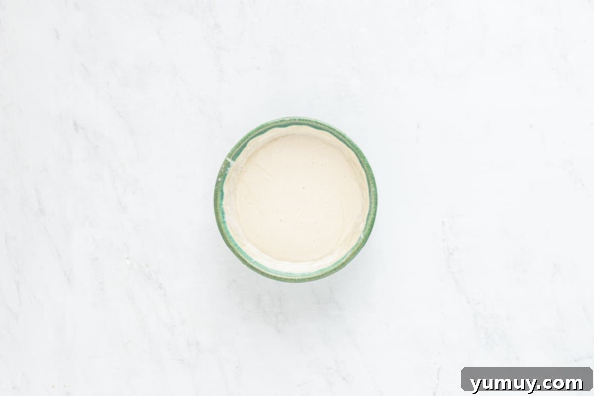 A bowl of smooth vanilla glaze on a marble surface, ready to be used for crullers.