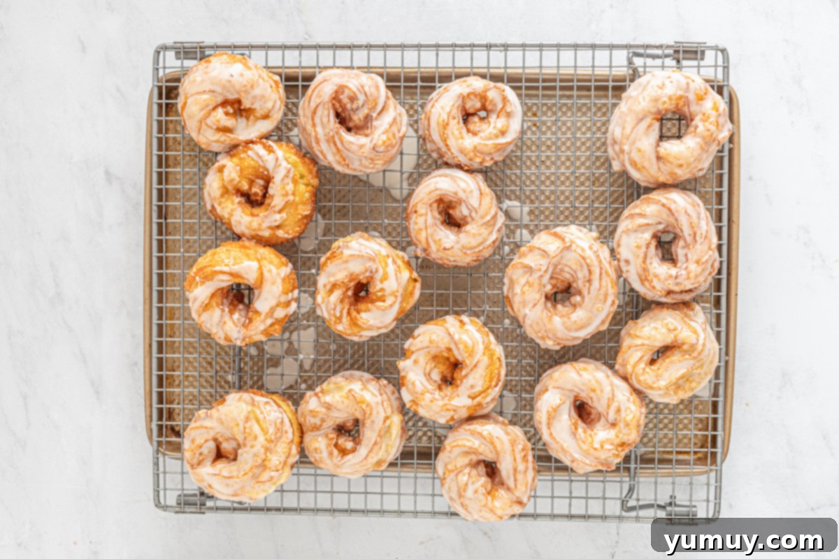 Rows of freshly glazed French crullers arranged on a wire cooling rack, allowing the glaze to set.