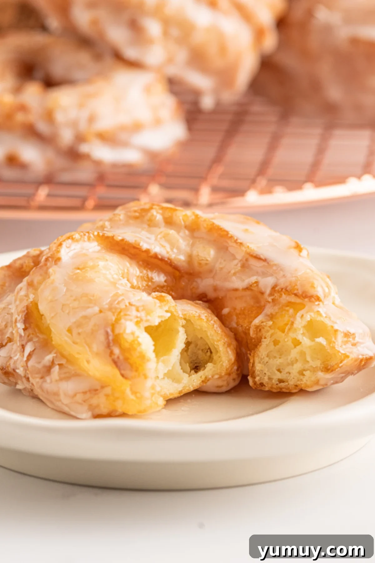 Close-up of a perfectly glazed French cruller on a white plate, highlighting its crisp texture and airy interior beneath the cracked vanilla coating.