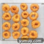 Freshly fried French crullers cooling on a wire rack after being removed from the oil.
