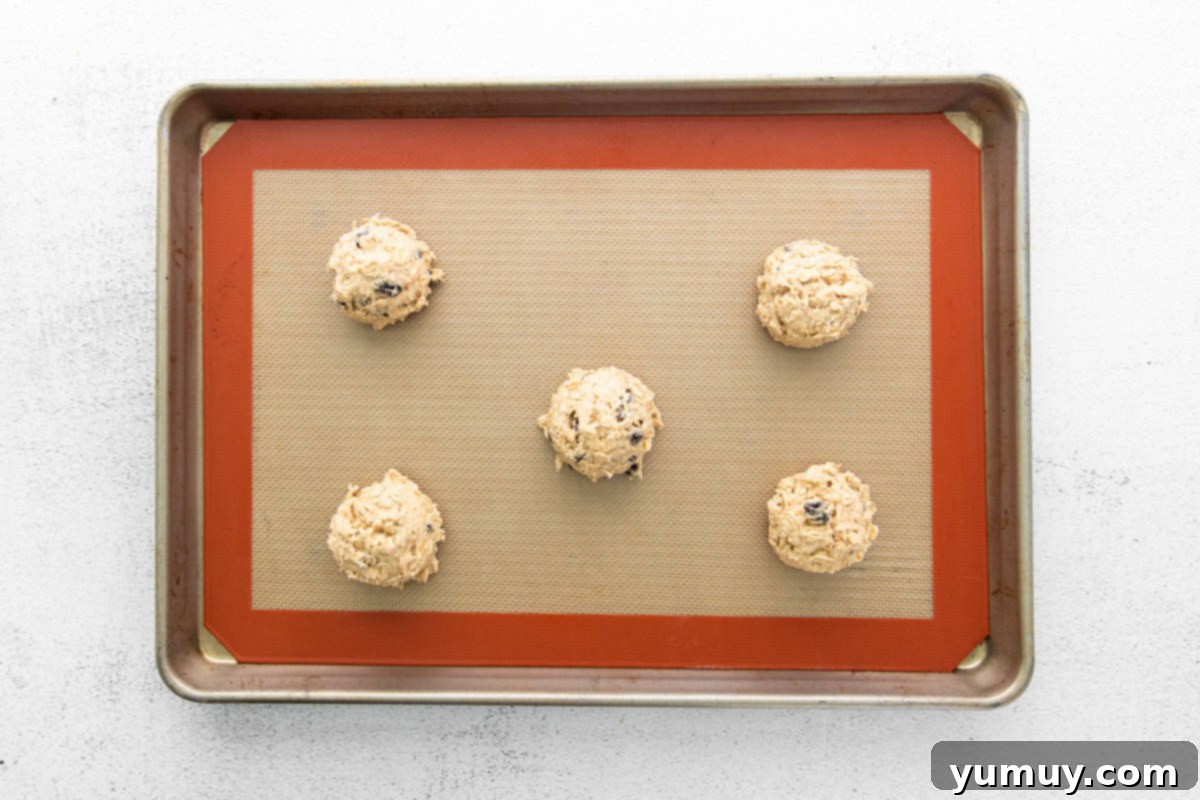 Golden Oat Raisin Delights 12 Neatly arranged balls of oatmeal raisin cookie dough on a parchment-lined baking tray, ready for the oven.