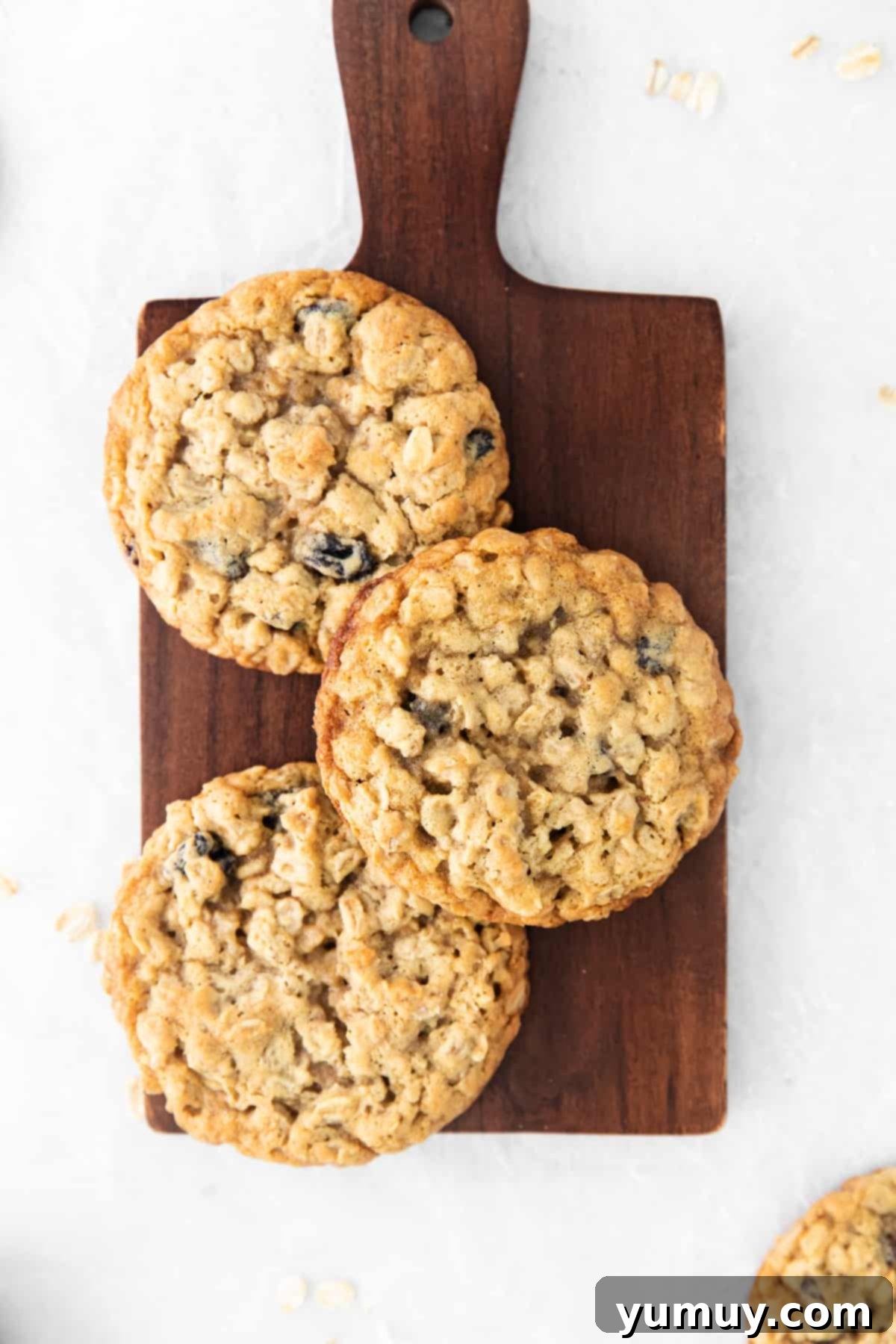 Golden Oat Raisin Delights 3 A rustic wooden cutting board laden with a tempting pile of freshly baked oatmeal raisin cookies, some stacked, others scattered.