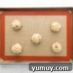 Golden Oat Raisin Delights 7 Balls of oatmeal raisin cookie dough perfectly arranged on a parchment-lined baking tray, ready for the oven.