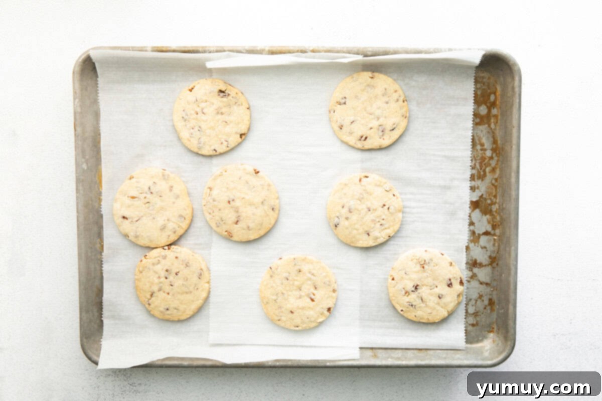 Melt-in-Your-Mouth Pecan Shortbread 7 freshly baked pecan shortbread cookies on a lined baking sheet.