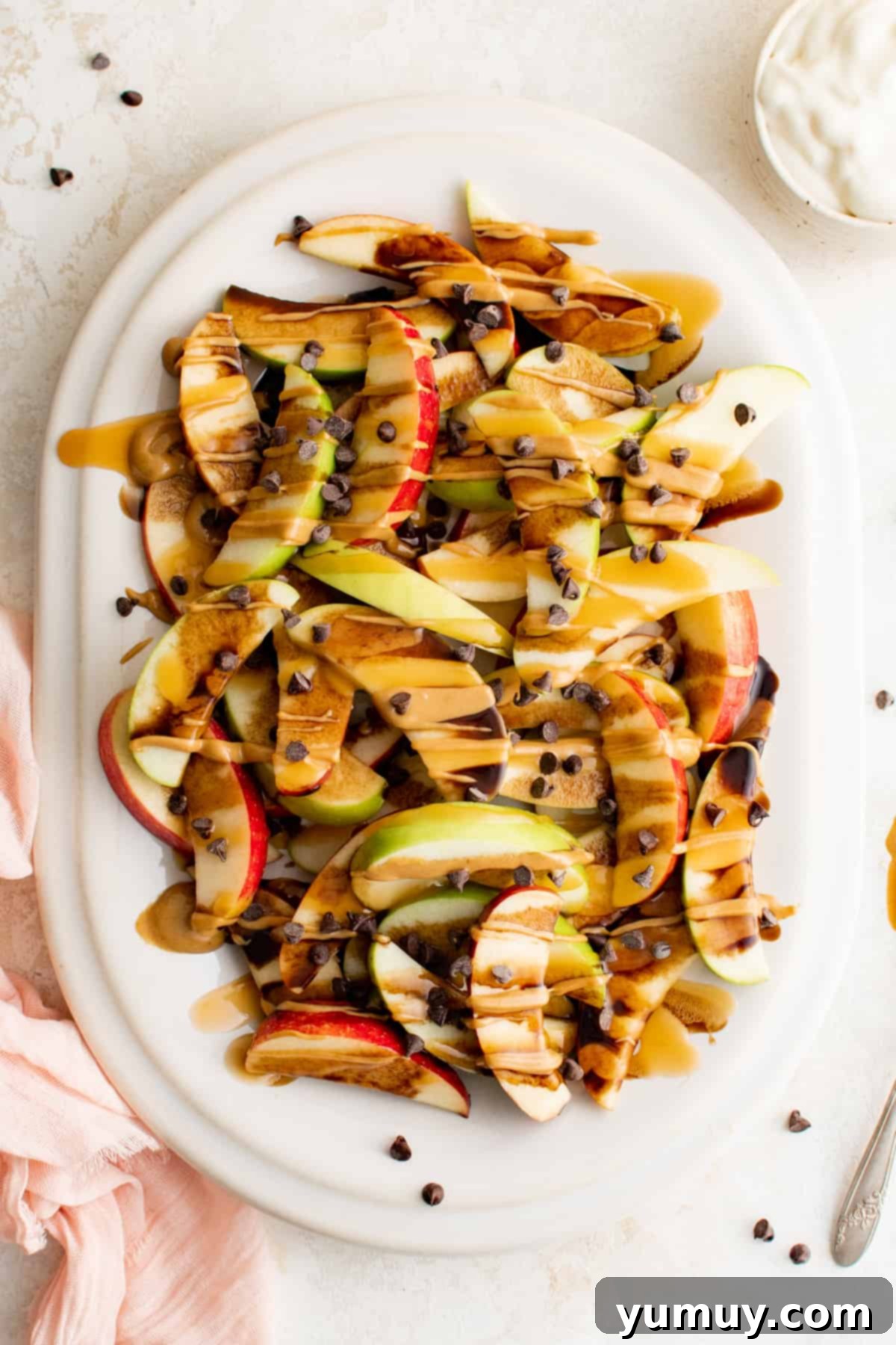 A vibrant platter of caramel apple nachos, featuring crisp apple slices generously topped with sweet caramel, rich chocolate, and creamy peanut butter drizzles, finished with mini chocolate chips.