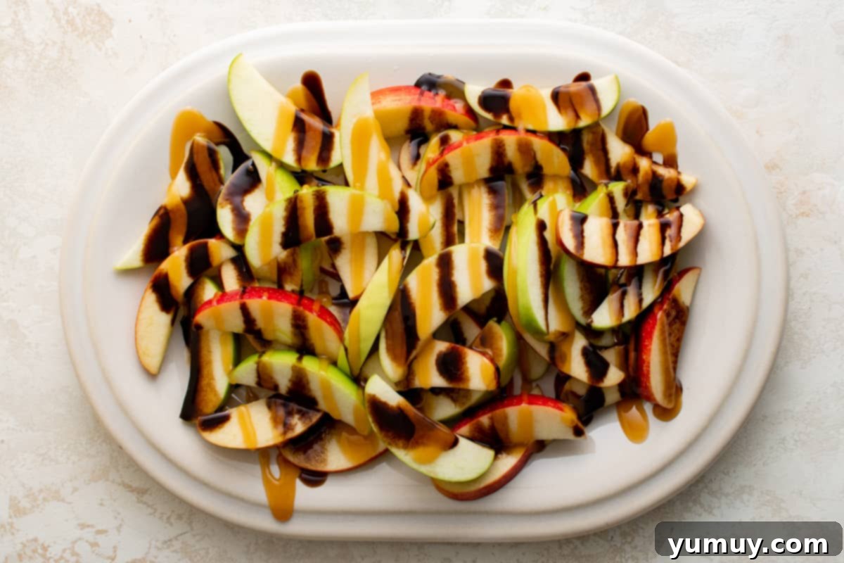 A close-up view of apple slices on a platter, being beautifully drizzled with luscious caramel and rich chocolate sauces, creating an inviting visual.