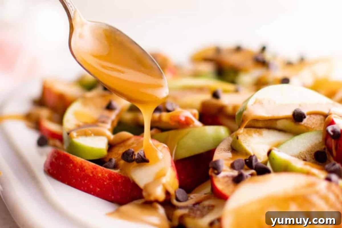 Close-up shot of rich caramel sauce being drizzled artistically over a colorful plate of apple nachos, already adorned with other toppings.