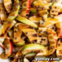 A beautifully arranged platter of caramel apple nachos, showcasing colorful apple slices coated in caramel, chocolate, and peanut butter, garnished with chocolate chips.