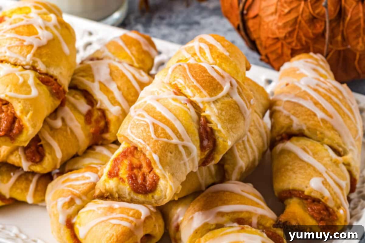 A serving tray of pumpkin pie crescent rolls, freshly glazed, presented on a table with a glass of milk and a decorative pumpkin.