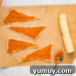 Triangles of crescent roll dough are laid flat on parchment paper, ready for filling.