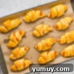 Pumpkin pie crescent rolls lined up on a parchment-lined baking tray before baking.