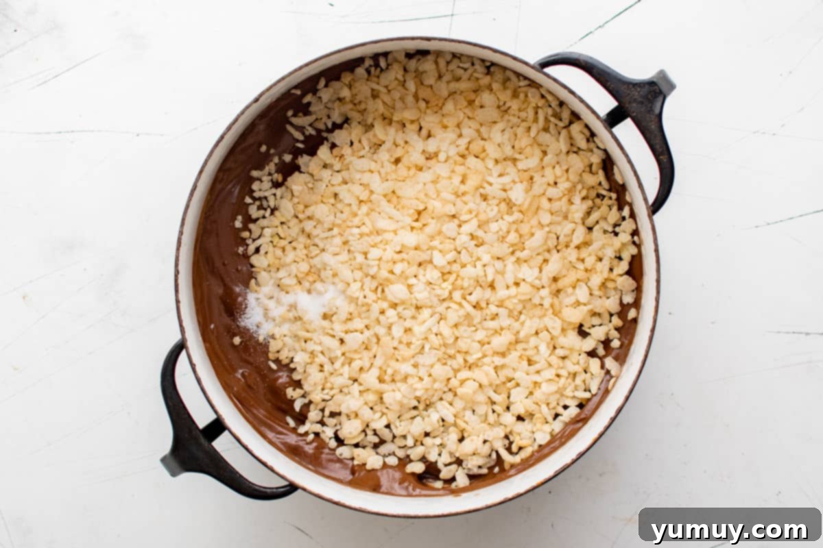 Irresistible Homemade Crunch Bars 12 Rice Krispies cereal being stirred into the melted chocolate in a Dutch oven.