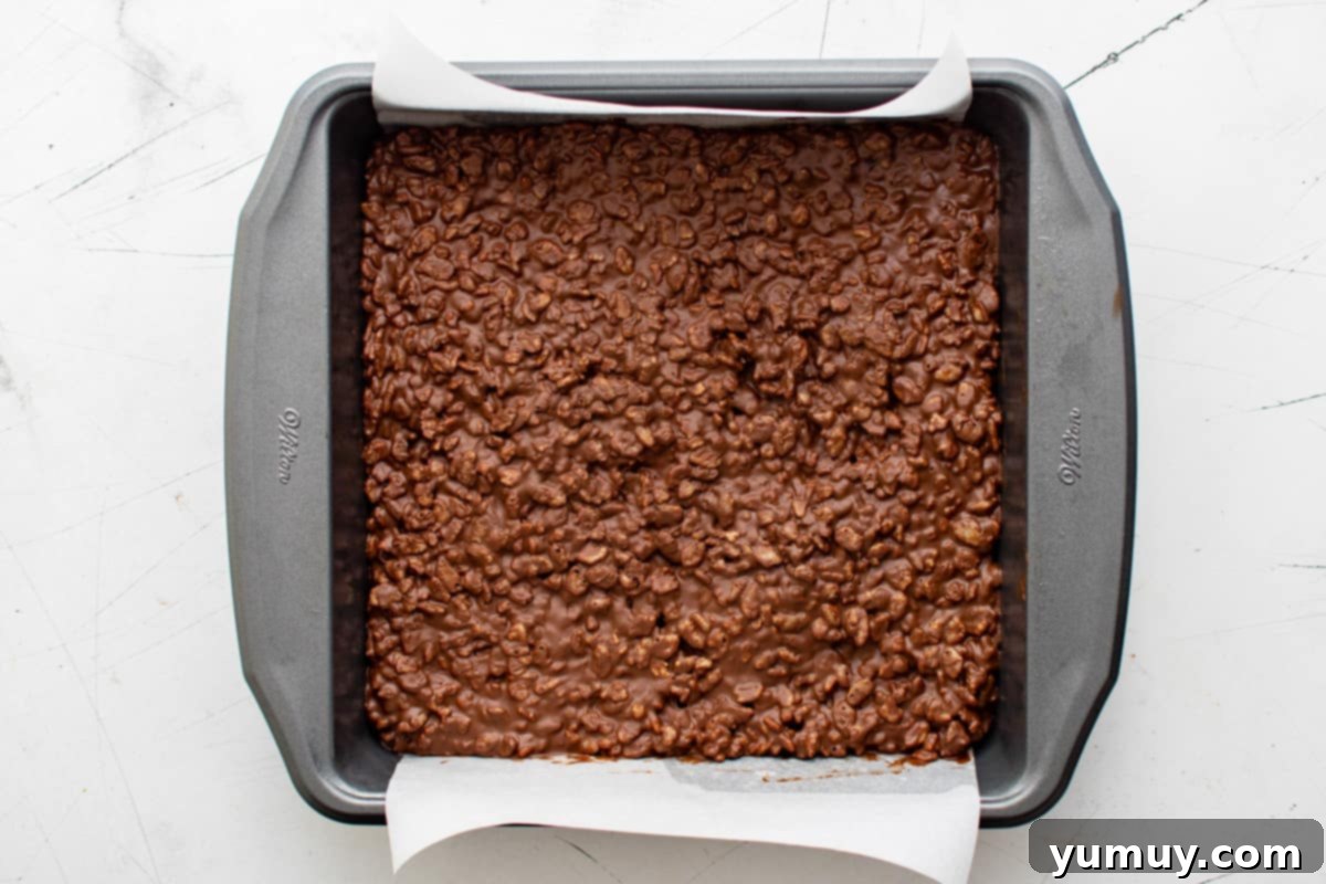 Irresistible Homemade Crunch Bars 14 Chocolate crunch bar mix spread out in an 8x8 baking pan, ready to cool.