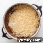 Irresistible Homemade Crunch Bars 6 Rice Krispies cereal being added to melted chocolate in a Dutch oven.