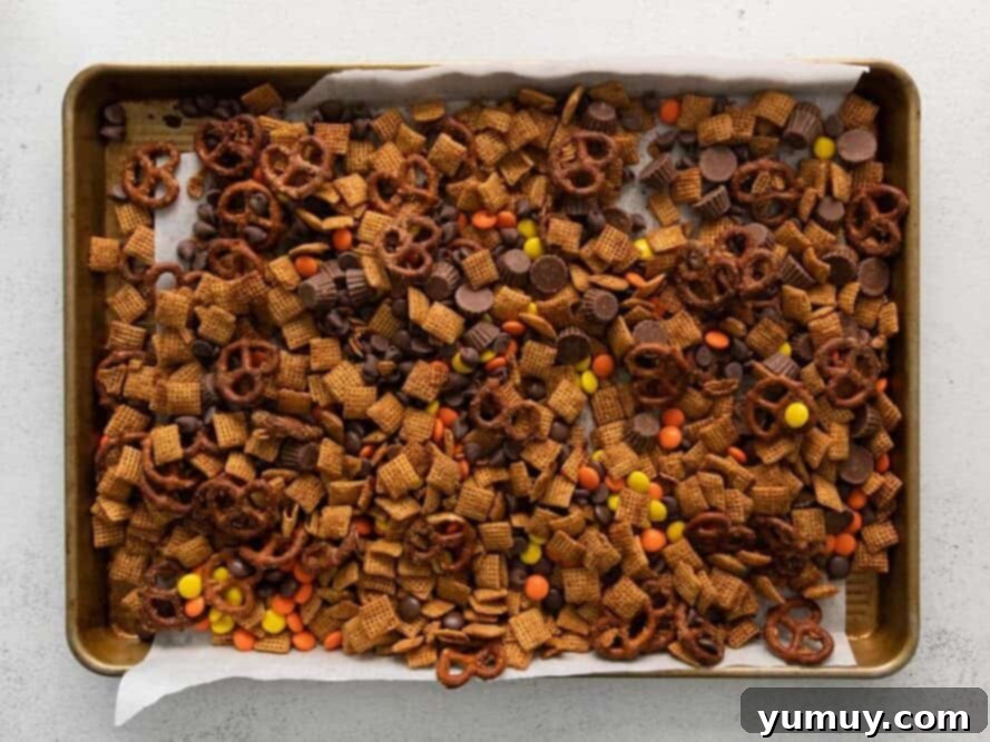 A baking sheet filled with the cooled Chex mix, now combined with Reese's Pieces, chocolate chips, and mini Reese's Cups.