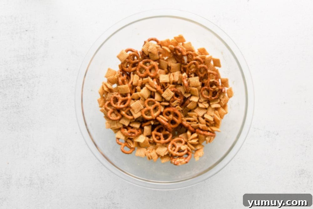 A close-up shot of pretzels and Chex cereal being tossed in a large bowl with a buttery sugar mixture.