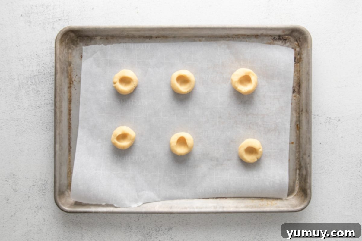 Caramel Chocolate Shortbread Cookies 14 Six perfectly shaped, unbaked shortbread cookie dough balls with clear thumbprint indentations, placed on a parchment-lined baking sheet.