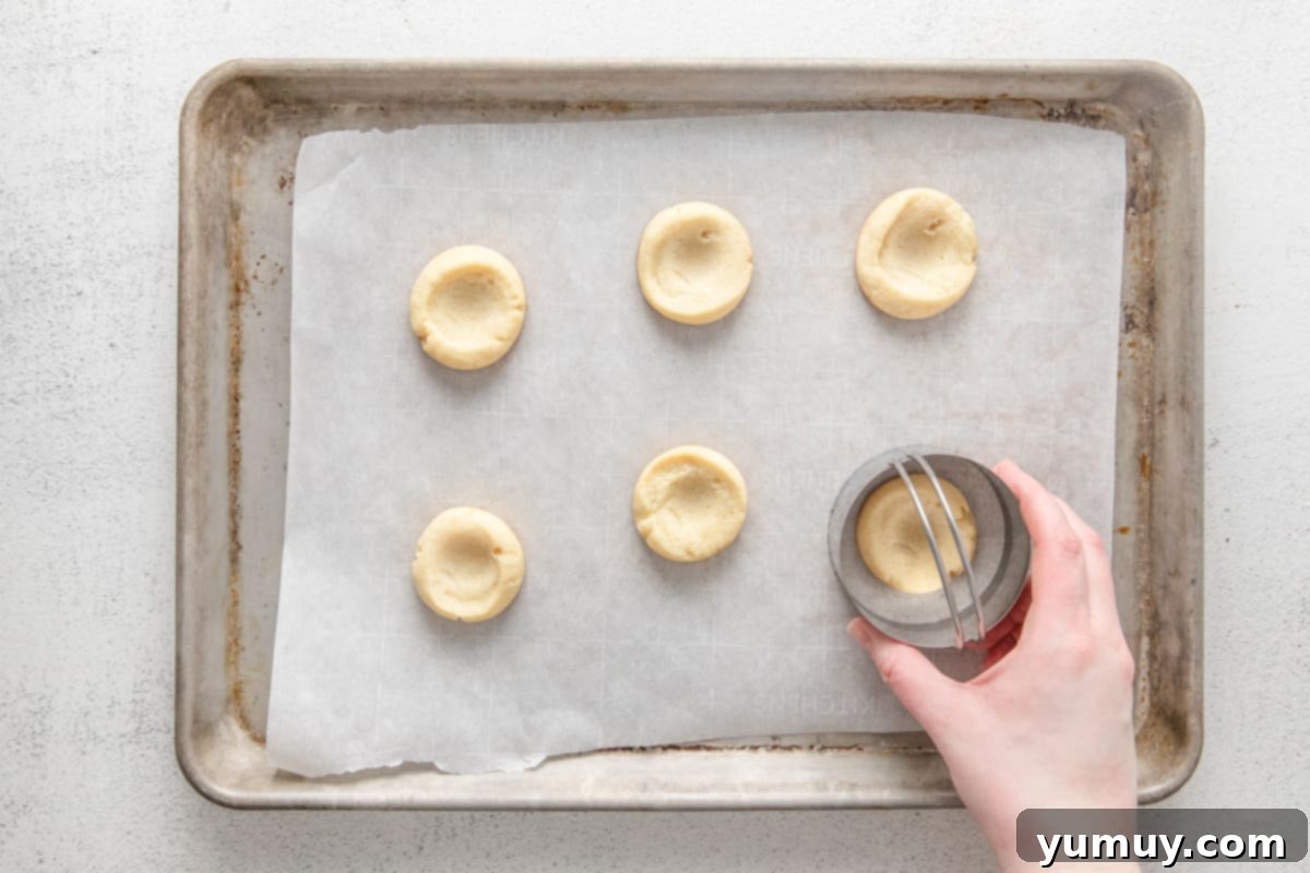 Caramel Chocolate Shortbread Cookies 15 A hand using a round biscuit cutter to gently reshape the edges of warm, baked shortbread cookies on a baking sheet, enhancing their circular form and thumbprint wells.