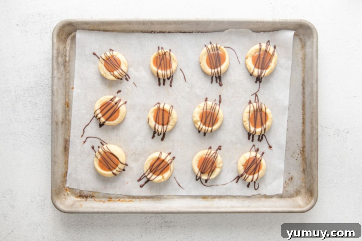 Caramel Chocolate Shortbread Cookies 18 A baker's dozen of finished Twix cookies arranged on a baking sheet, each with a perfect caramel center and elegant chocolate drizzle, topped with flaky sea salt.