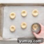 Caramel Chocolate Shortbread Cookies 8 A hand using a round biscuit cutter to reshape the edges of baked shortbread cookies on a baking sheet, defining the thumbprint indentation.