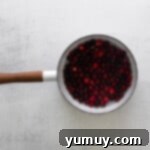 Tangy Cranberry Delights 6 Cranberries coated in syrup cooking in a saucepan.