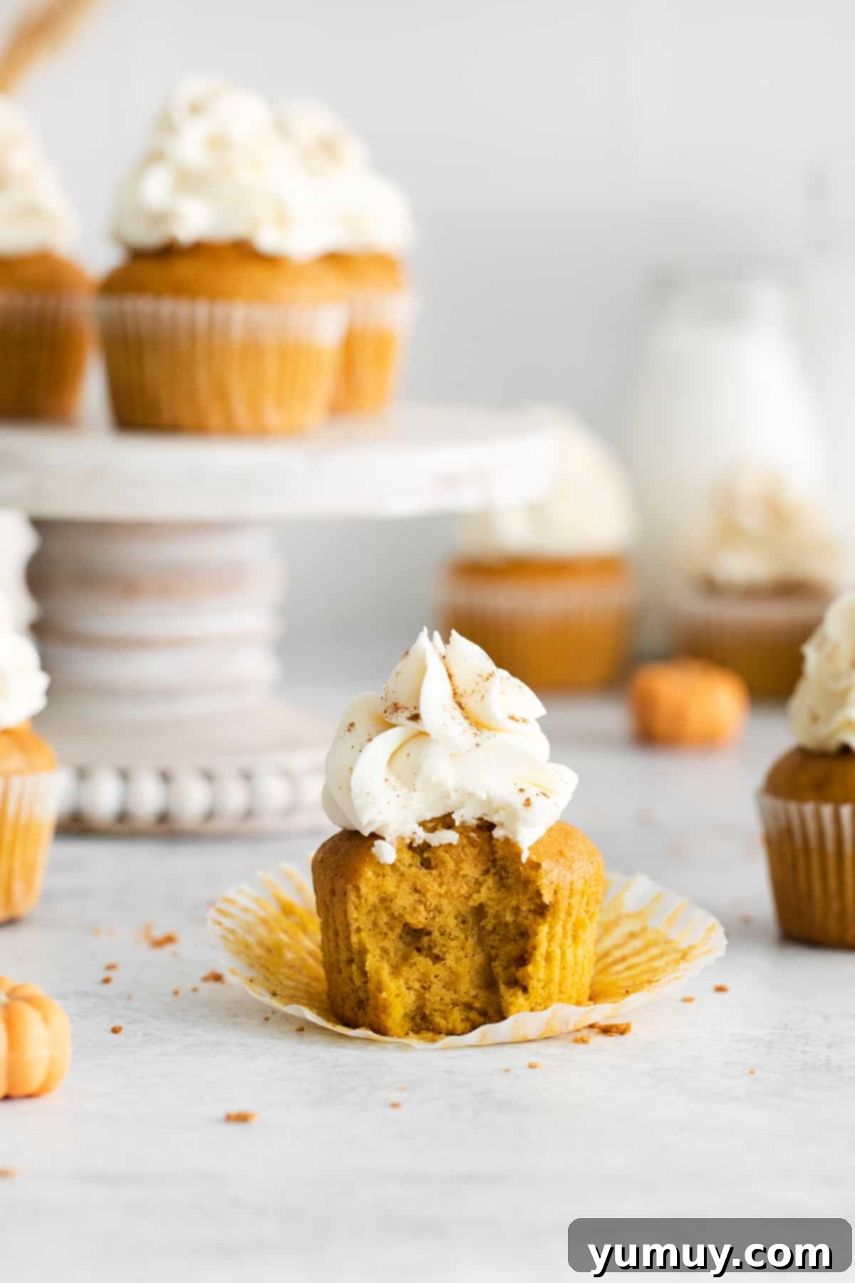 A beautifully frosted pumpkin pie cupcake with a bite taken out, revealing its creamy pumpkin filling, surrounded by more inviting cupcakes.