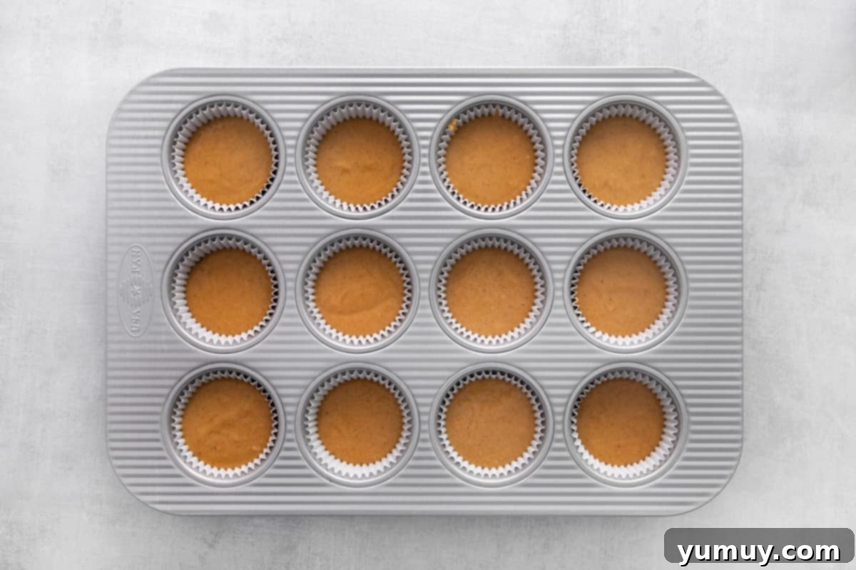 A cupcake tin with each well accurately filled ¾ full with pumpkin cupcake batter.