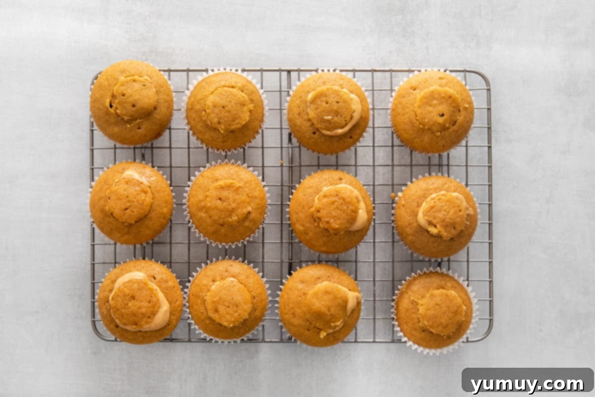 Cored cupcakes, some filled with pumpkin mixture and topped with the removed cake piece, on a cooling rack.