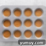 Cupcake tin with wells partially filled with pumpkin batter, ready for baking.