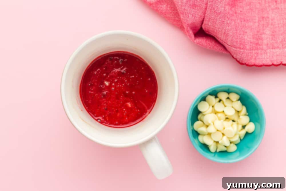 Red velvet cake batter mixed in a mug, alongside a small bowl of white chocolate chips ready to be added.