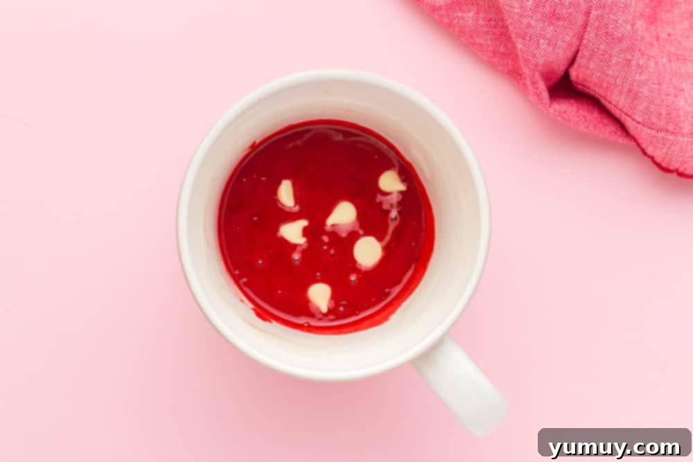 Smooth red cake batter filled with white chocolate chips in a mug, ready for microwaving.