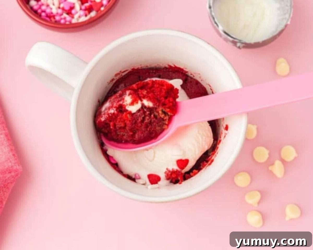 Pink spoon resting in a freshly microwaved red velvet mug cake, ready to be enjoyed.