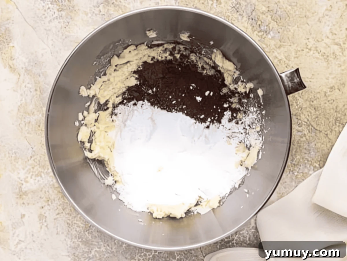Decadent Chocolate Cream Cheese Frosting 7 powdered sugar and cocoa powder over whipped butter and cream cheese in a stand mixer bowl.