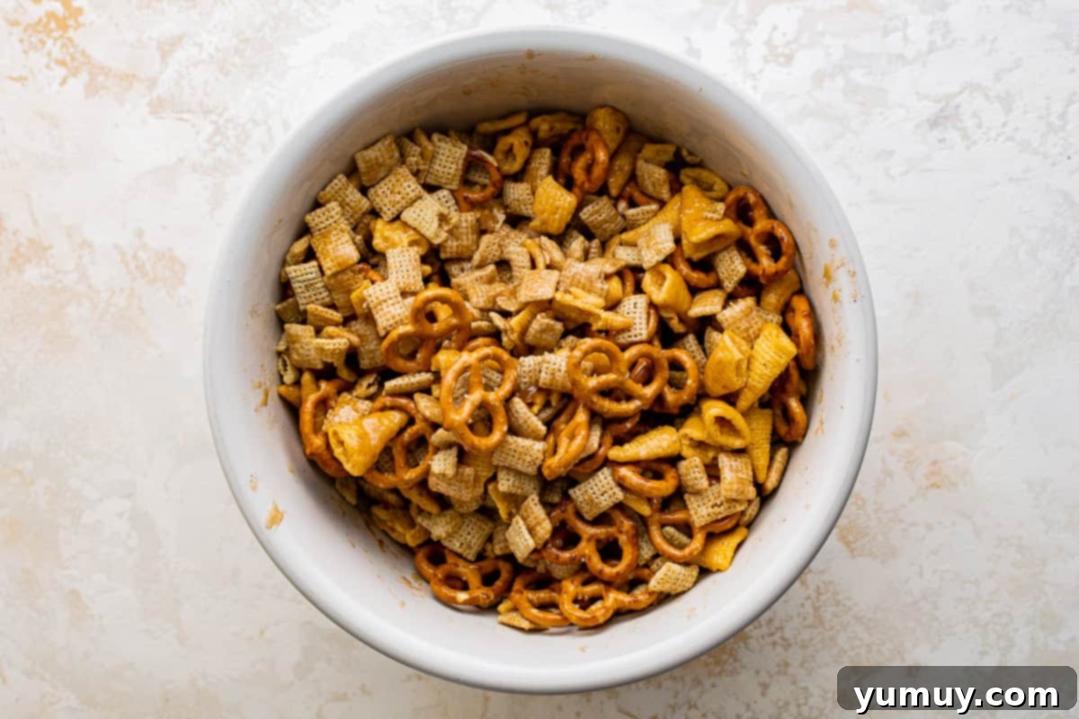 chex cereal, mini pretzels, and bugles in a large white bowl drizzled with spiced butter.