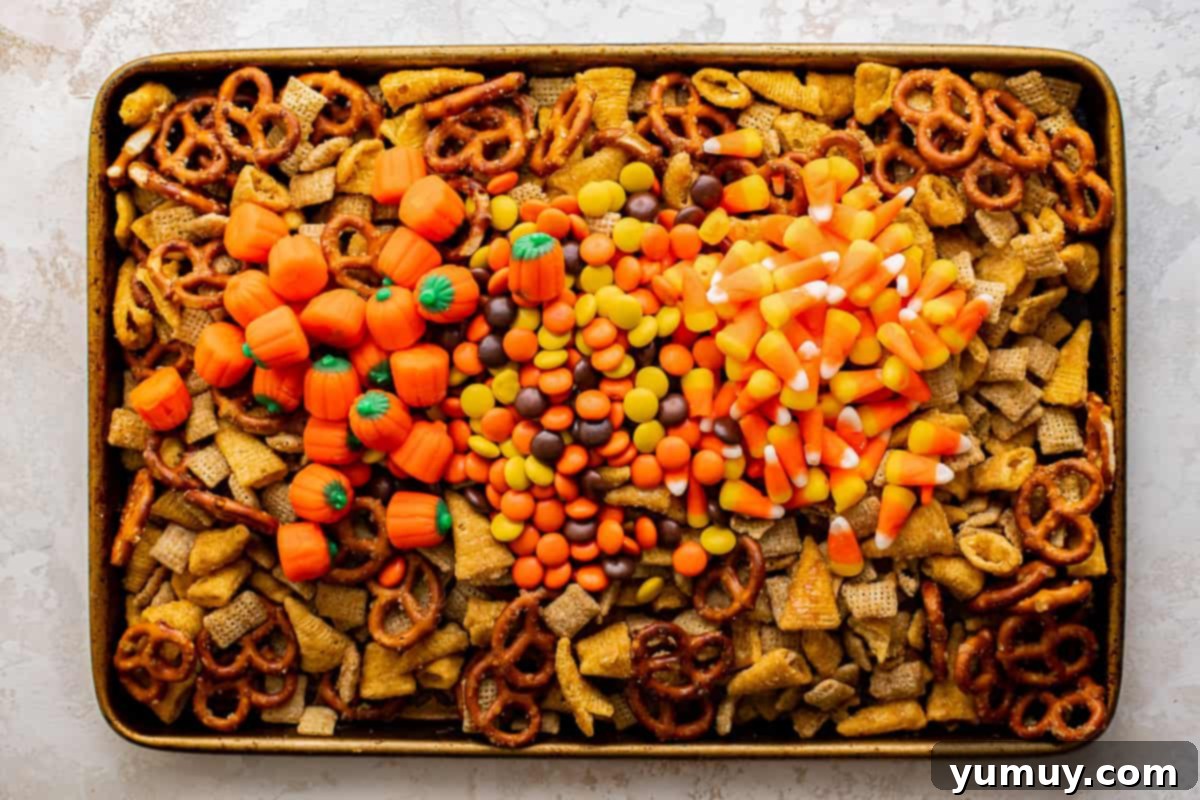 baked halloween chex mix on a baking sheet topped with pumpkin candies, candy corn, and reese's pieces.